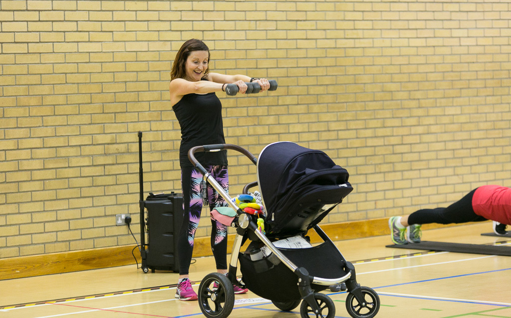 Mum holding weights beside child's buggy